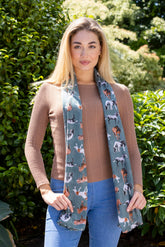 A woman wearing a green lightweight polyester scarf with a horse pattern, paired with a brown top and blue jeans.